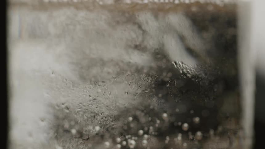 A beverage is poured into a glass creating a series of bubbles