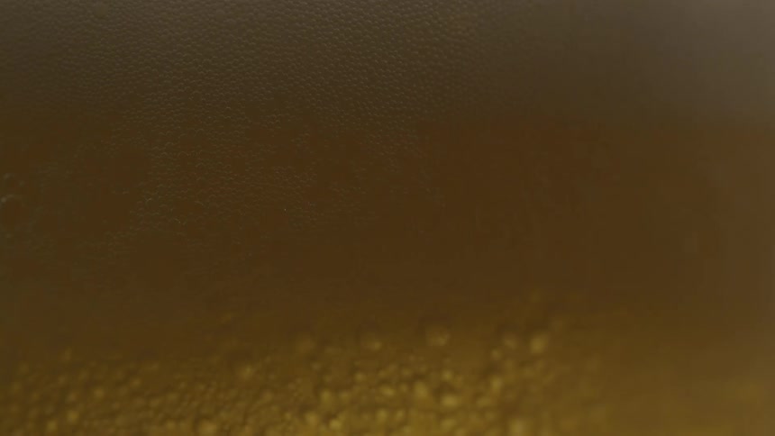 A closeup of foamy bubbles rising atop a golden carbonated beverage