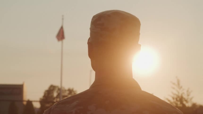 Soldier watches the american flag waving at sunset