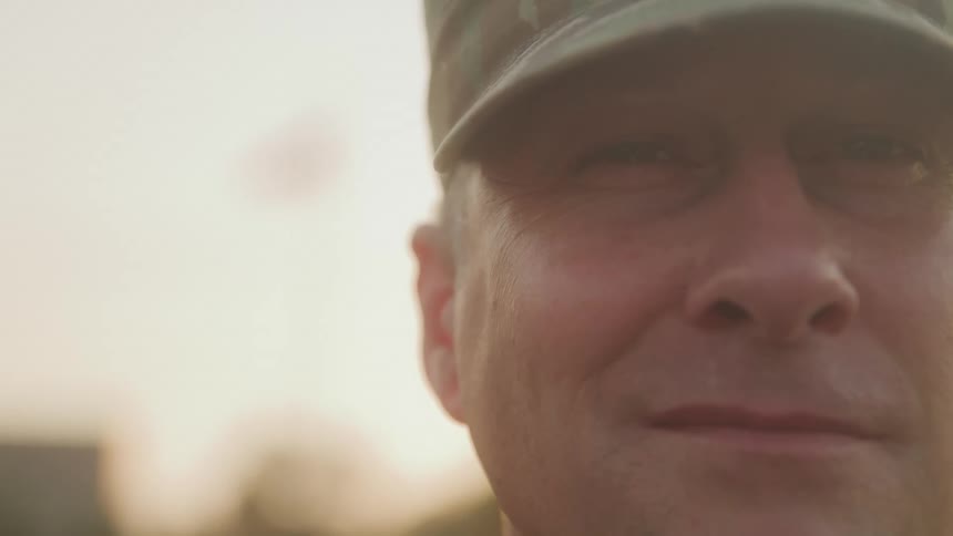 A military officer wearing a military hat smiles outdoors