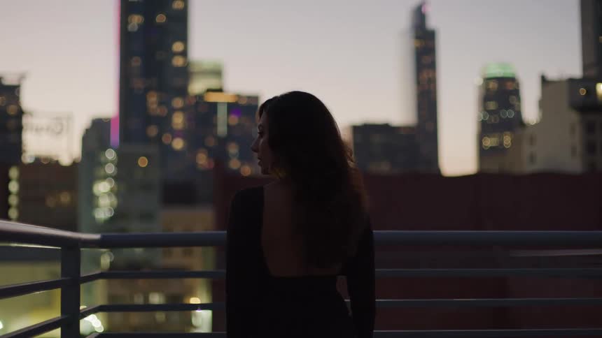 Woman stands at the corner of a rooftop railing and gazes at the city around her