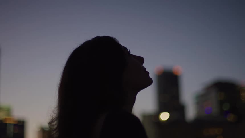 A young woman standing on the rooftop of a building at dawn enjoying the fresh air with the cityscape in the background