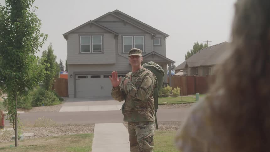 The video filmed from a firstperson perspective shows a man in military uniform with a large duffel bag on his shoulder walking away from a house he turns and waves goodbye before continuing down the driveway