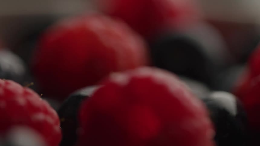 Fresh raspberries and blueberries are captured in a tight closeup with soft lighting