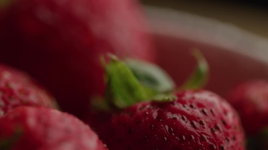 The video displays a closeup of vibrant red strawberries with water droplets clinging to their surface the focus is on the intricate details of the fruit including their tiny seeds and green leafy tops