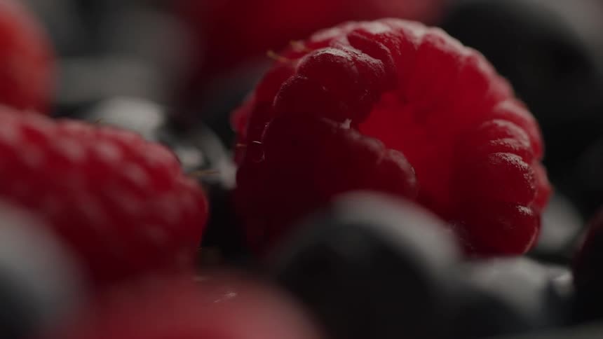 Extreme close up of a red ripe raspberry on top of blueberries