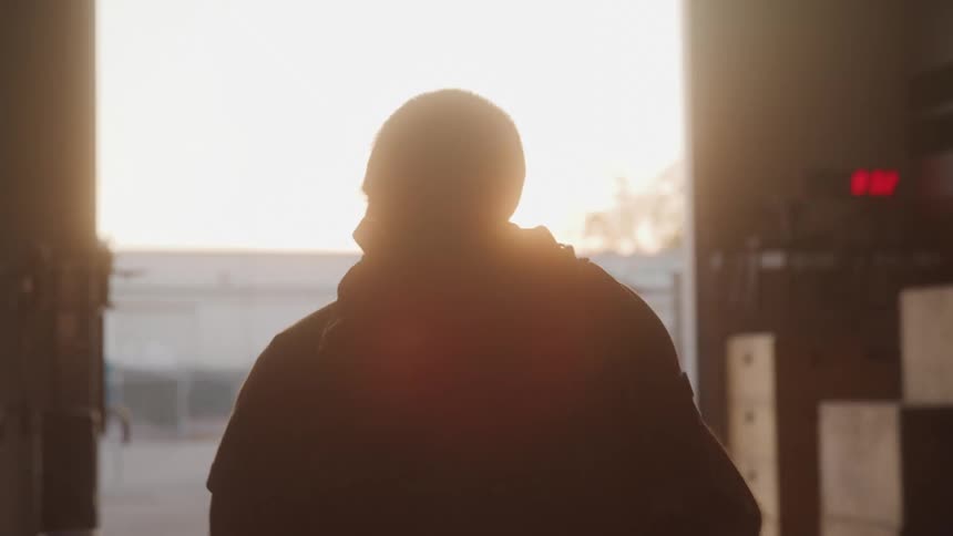 A person with a backpack is walking away from the camera silhouetted against a bright sunny entrance the light creates a strong glare around their head and shoulders