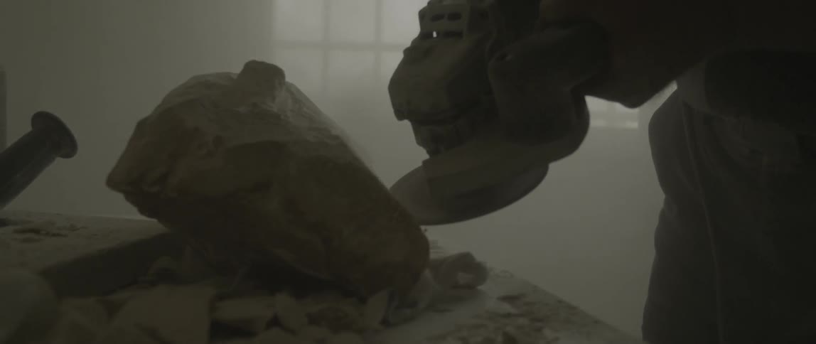 A man uses a power tool to shape a rock