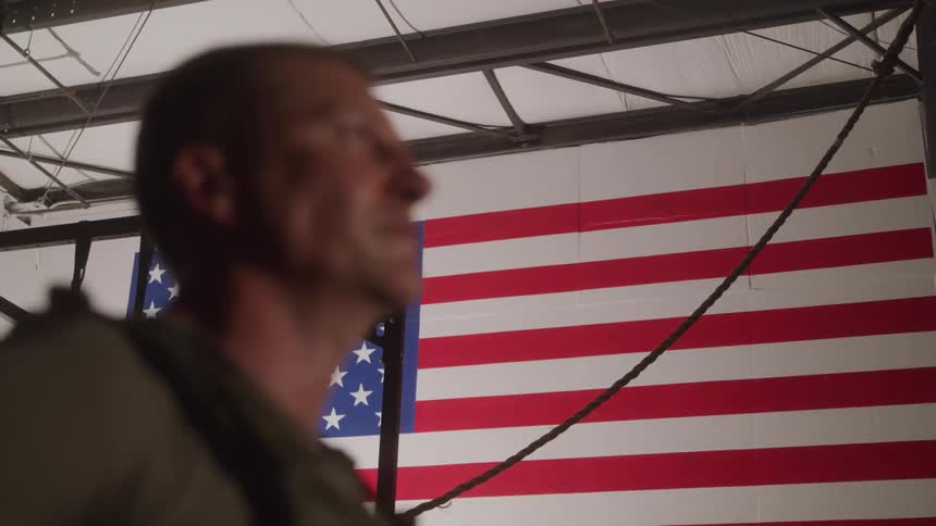 The man is standing in front of an american flag on the wall