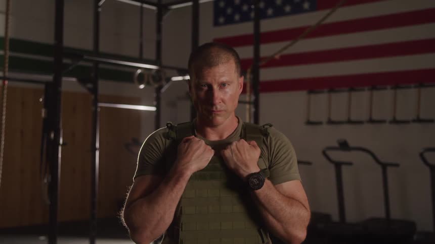 The soldier is holding onto his bullet proof vest