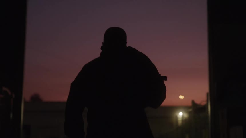 A man slings a backpack on his back as he walks outside