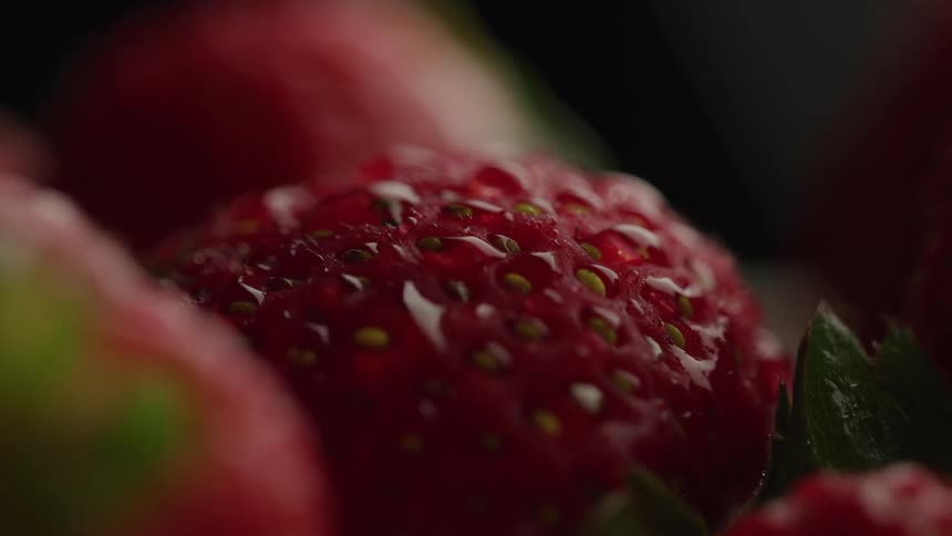 Close up of a strawberry covered in water droplets lying beside other strawberries