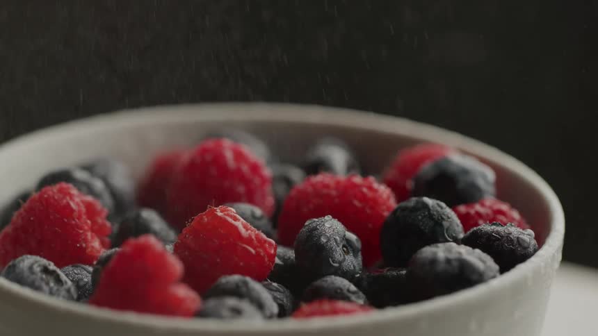 A closeup shot of a white bowl filled with a mix of red raspberries and dark blueberries appearing lightly frosted