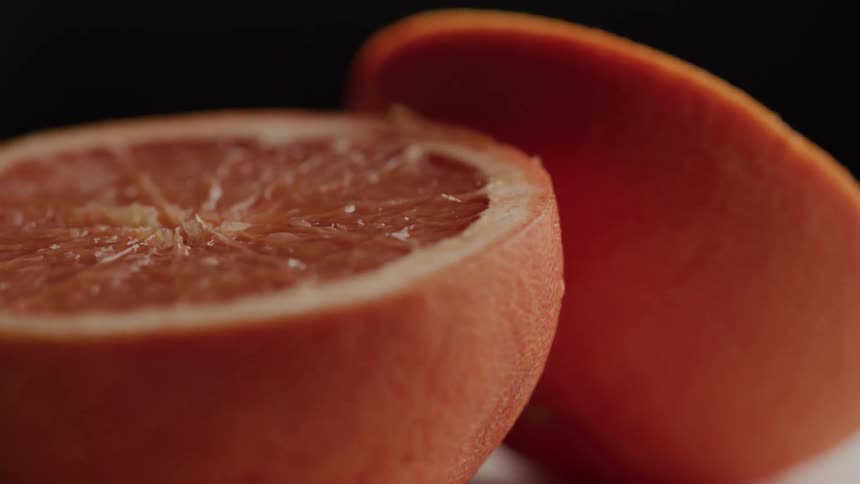The video shows two halves of a grapefruit on a dark surface with the camera slightly zooming in the juicy texture of the fruit is clearly visible