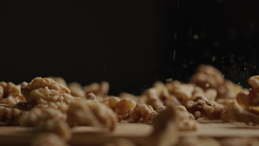 Numerous walnut without shells are dropped from above onto a wooden surface