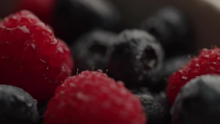 Fresh raspberries and blueberries are captured in a tight closeup with soft lighting