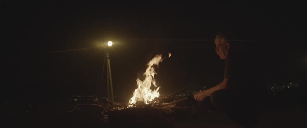 A man sits at a campfire at night