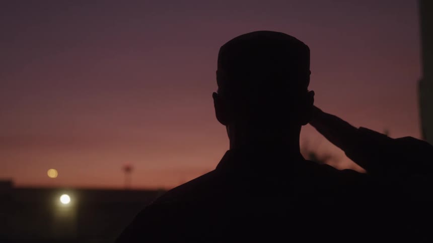 Close up silhouette of a male military personnel saluting while standing outdoors at dusk