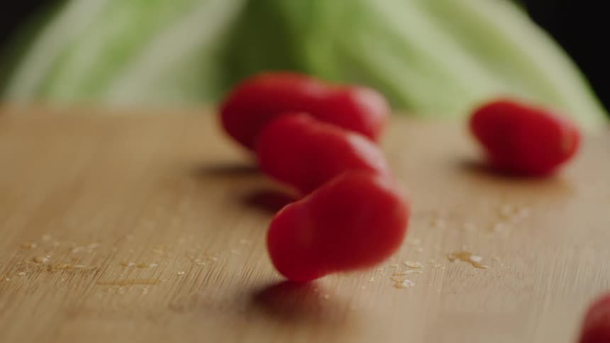 Grape tomatoes bounce off a wooden surface scattering water droplets