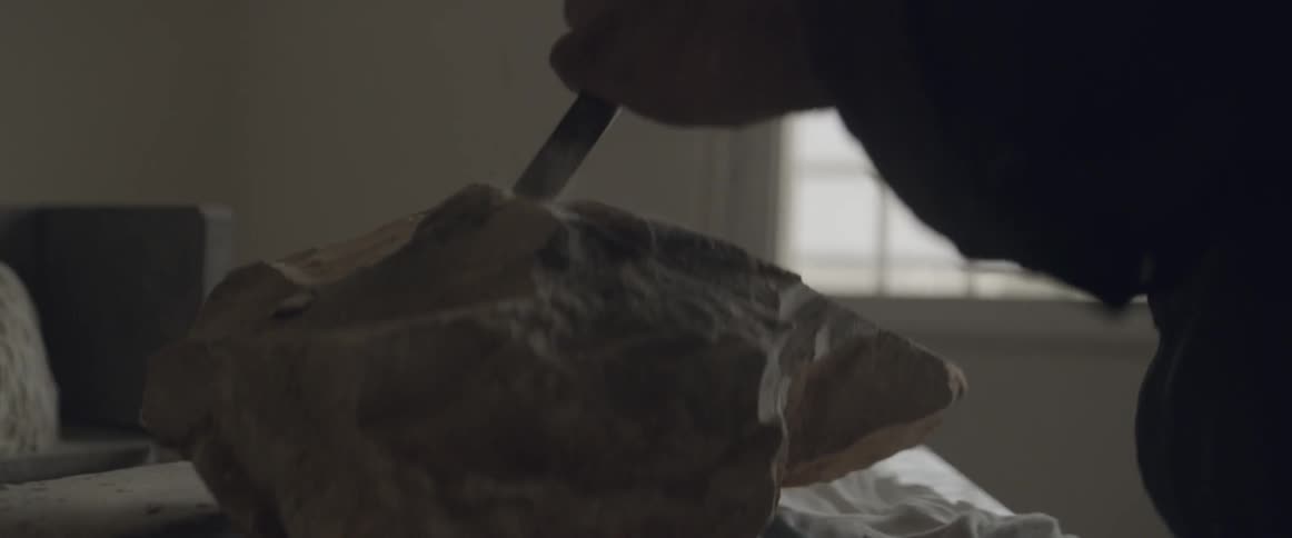 A man uses a hammer and chisel to shape a stone