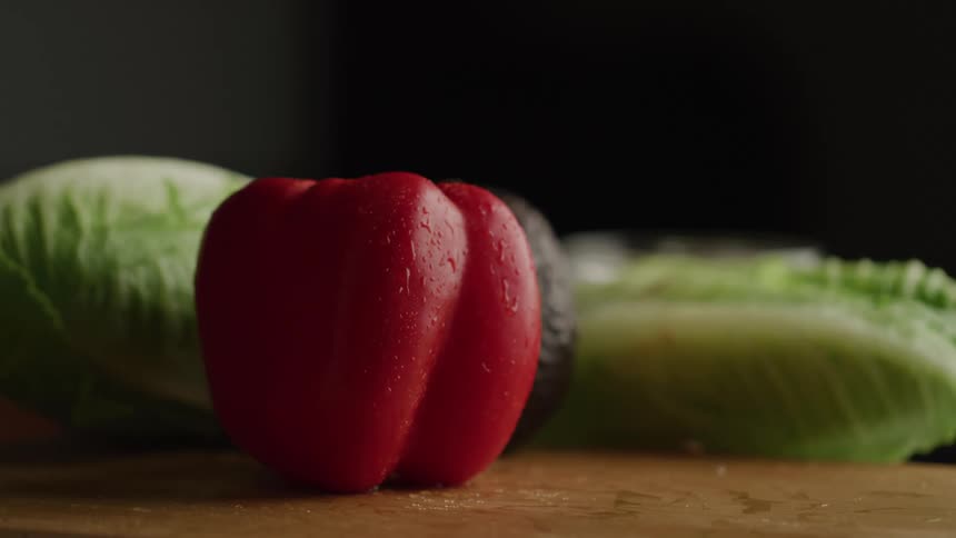 A red pepper lands in front of lettuce and an avocado