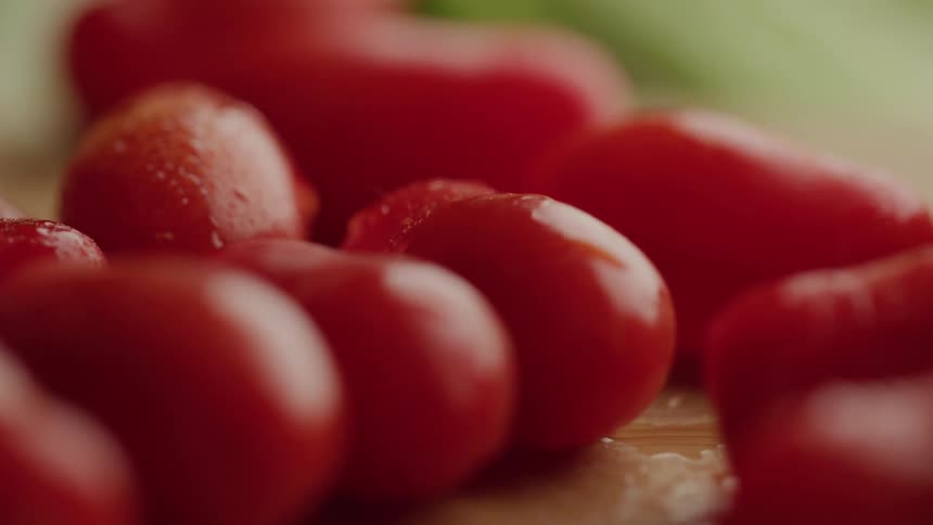 A pile of wet cherry tomatoes glistens with water droplets while some tomatoes fall