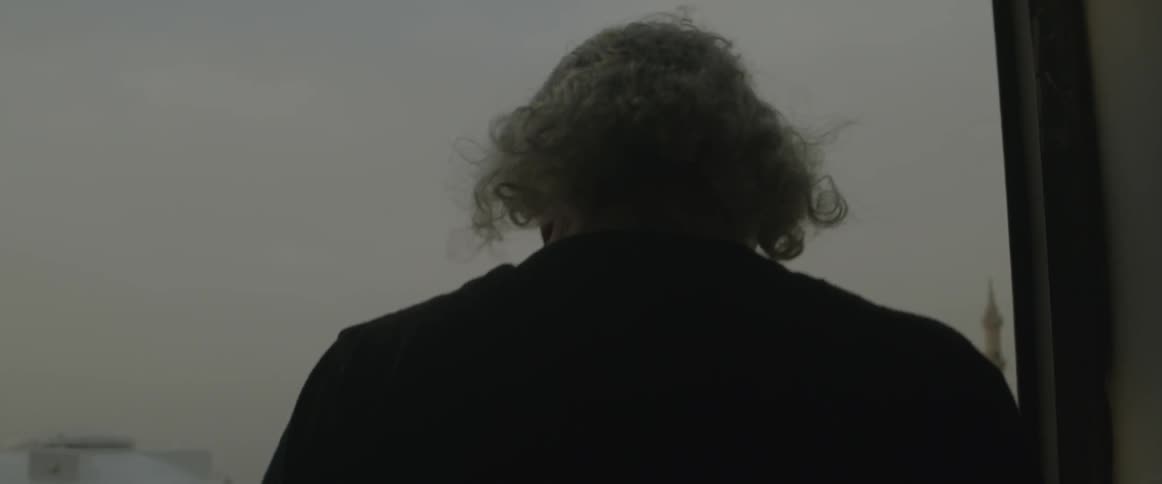 A man with glasses standing out on a balcony area looking over the town