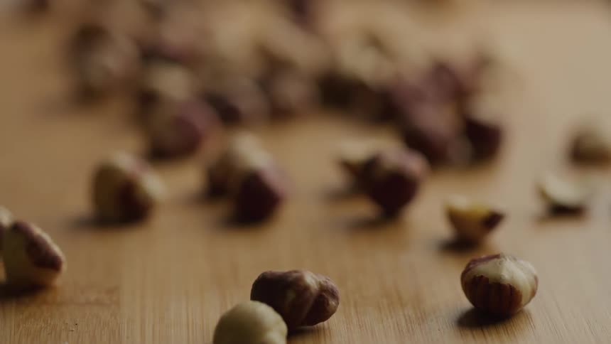 A series of hazelnuts scattered on a wooden surface at midday