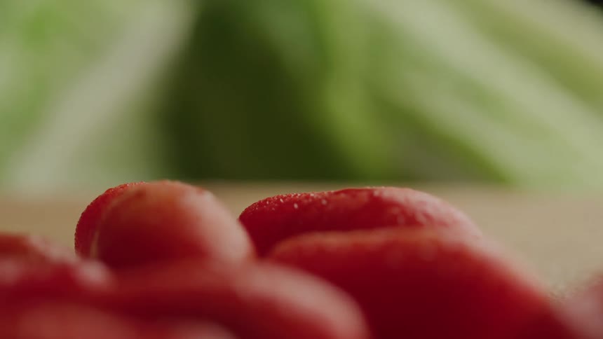 A close view focuses on several red plump tomatoes in the foreground with crisp green lettuce leaves blurred in the background all resting on a light brown surface