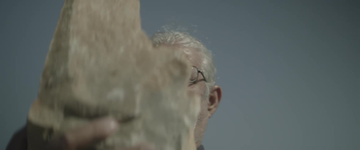 A man holds up a large rock on a clear sunny day