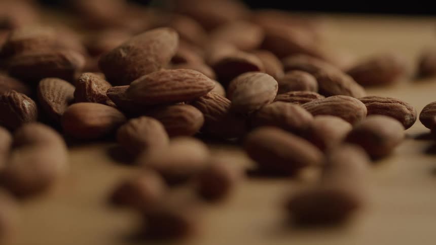 A scattered pile of whole almonds rests on a wooden surface in soft lighting
