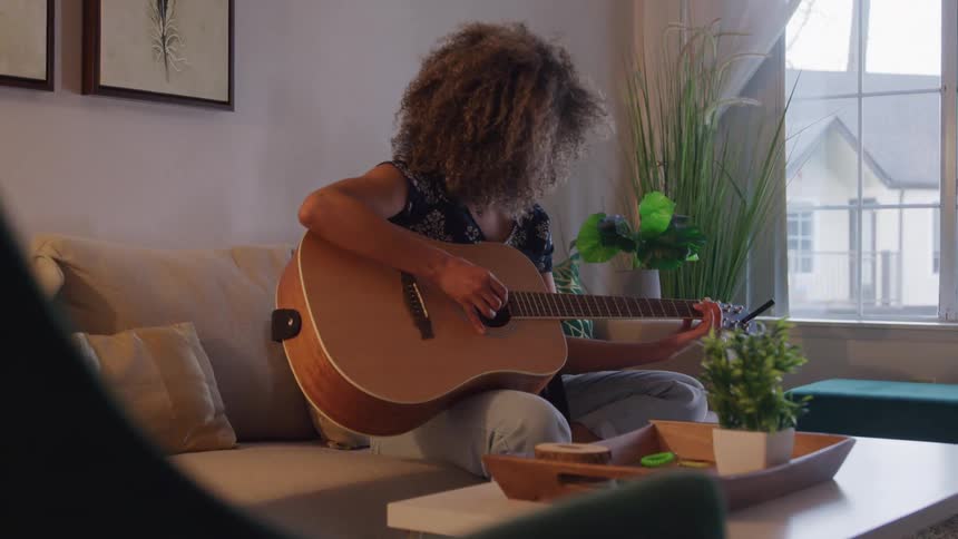 Woman with curly hair sitting playing guitar