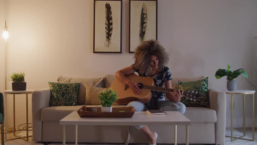 A woman sits on her couch and strums the guitar