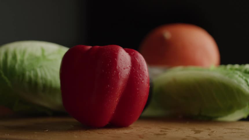 Wet red bell pepper dropping next to an avocado and lettuce on wood counter