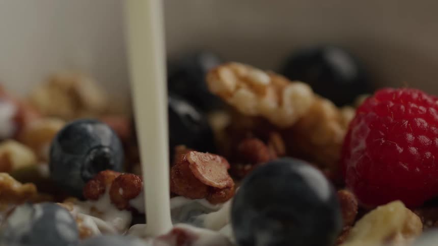 Milk pours over a colorful mix of berries nuts and granola