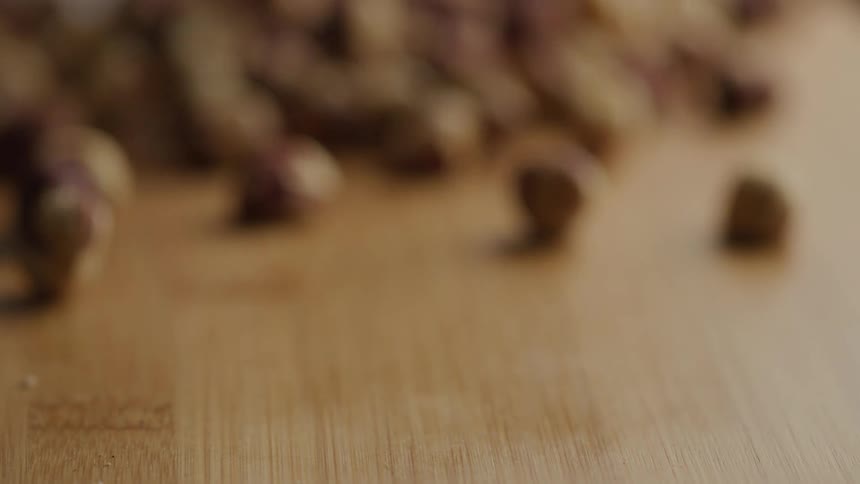 Hazelnuts roll in sharp focus on a wooden surface separated from a blurred pile in the background