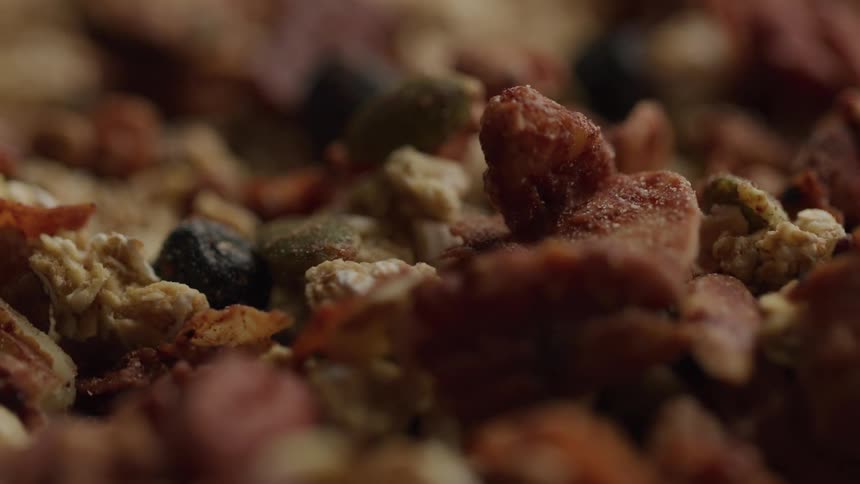 A closeup of mixed granola clusters seeds and dried fruit in soft warm lighting