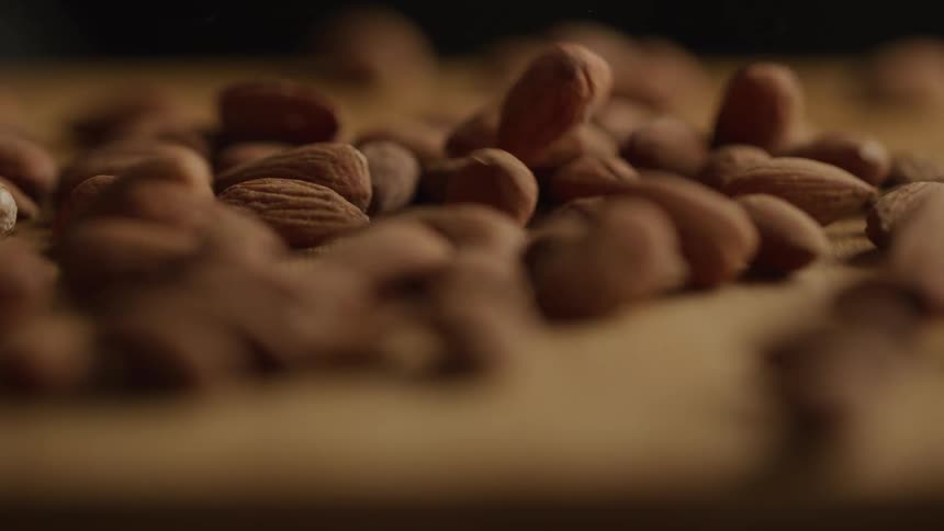 A scattered pile of raw almonds lies on a wooden surface with a shallow depth of field highlighting a few nuts in the center