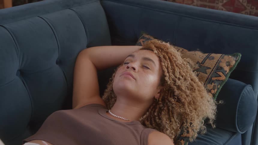 Young woman relaxes on couch gazing upward thoughtfully