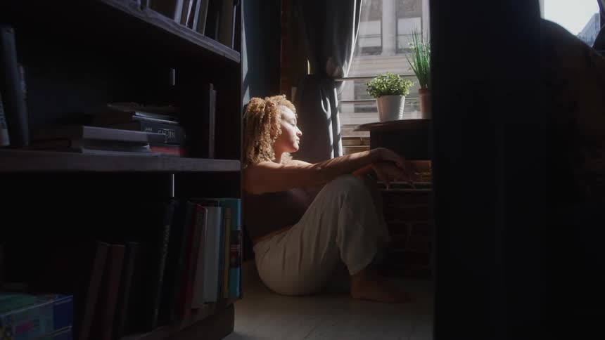 Sad woman sits by window lost in deep thought