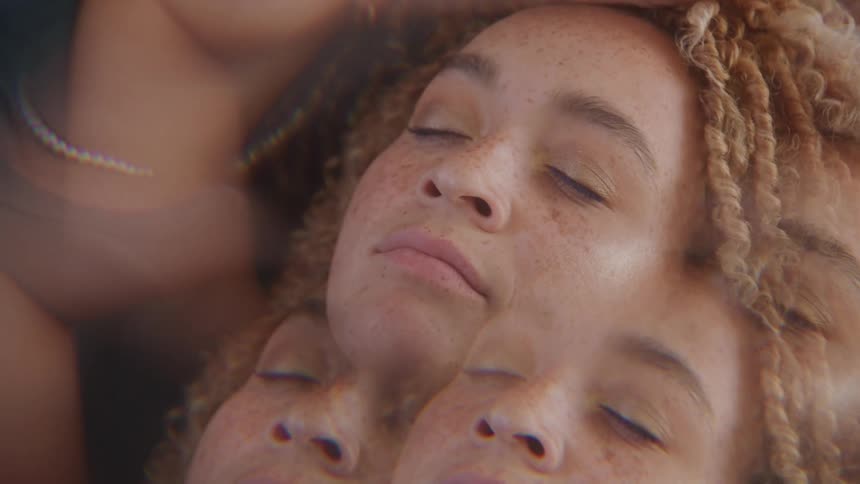 A serene woman with closed eyes and curly hair is shown in a dreamy kaleidoscopic overlay effect that duplicates her peaceful expression