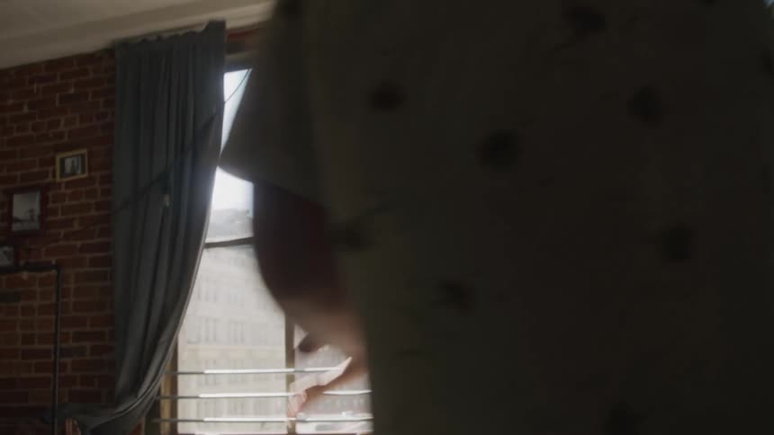 The video opens with a person in a dark blue top and lightcolored pants walking through a doorway they move towards a bright windowa man and a woman are then seen standing in front of the large window appearing to be in a heated discussion