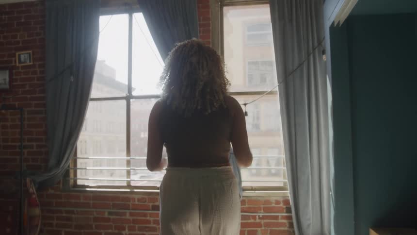 A woman walks through a residence before placing her hands on a window