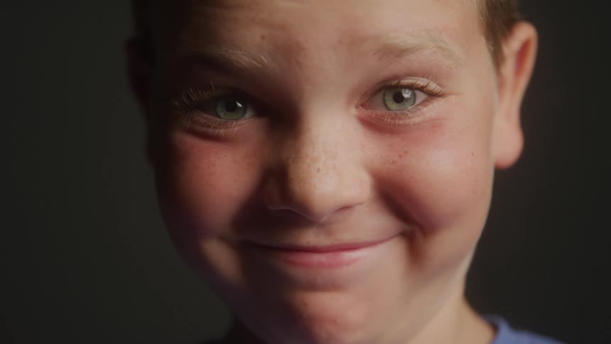 The video shows a closeup of a young boy with bright light green eyes looking directly at the camera he smiles revealing dental braces on his upper and lower teeth