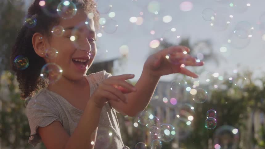 Girl smiles while playing with soap bubbles in the sunlight