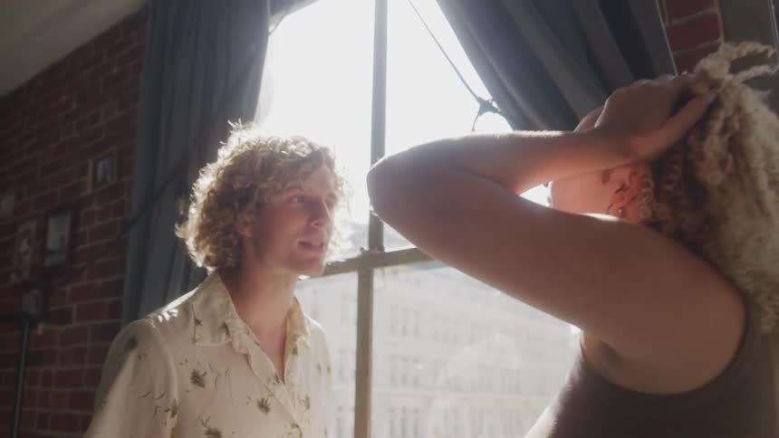 Man and a woman arguing next to a window in a room of the house