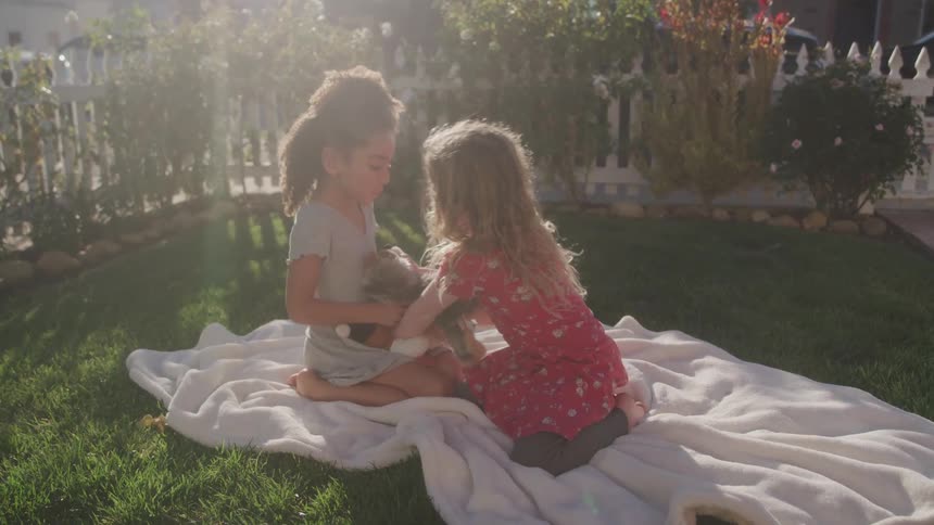 Two young girls play with stuffed dog on backyard blanket