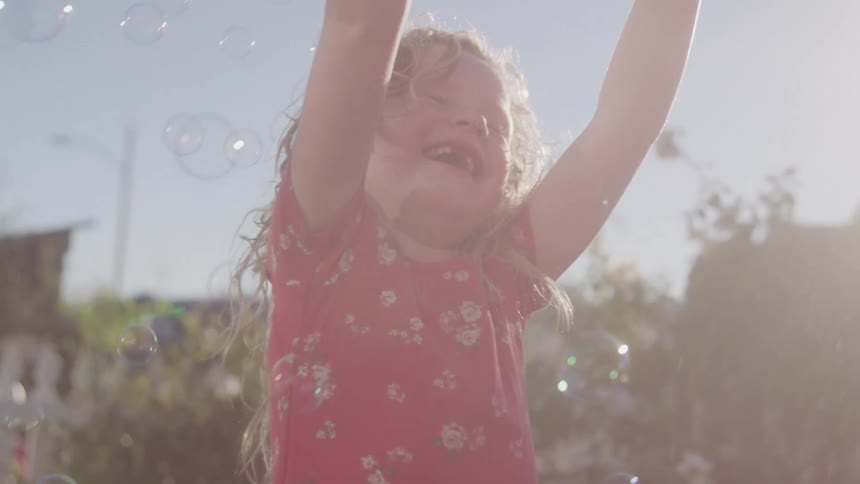 The girl is reaching up at the bubbles