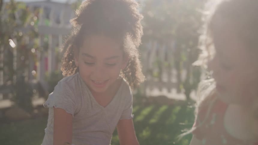 Two young girls play together in a sunlit garden their faces glowing with joy as soft afternoon light filters through the trees