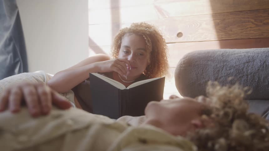 Man lying in bed next to a woman who is reading a book